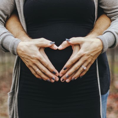 couple with heart shaped hands formed over pregnant belly